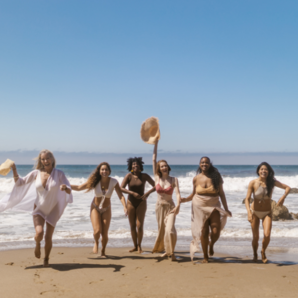 A group of women, running on the beach thriving and living their best life.